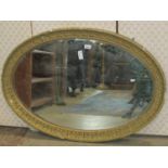 An antique gilt framed wall mirror of oval form with bevelled edge plate and repeating foliate