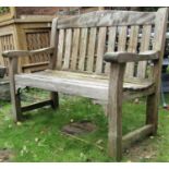 A weathered teak two seat garden bench with slatted seat and back beneath an arched rail, (af) 125cm