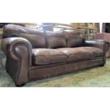 A substantial good quality sofa upholstered in a mid brown coloured leather with scrolled arms, stud