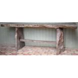 A nicely weathered/silvered rough hewn forest art garden table with planked top raised on a pair