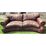 A substantial good quality sofa upholstered in hide in a mid tan colour with concave outline and