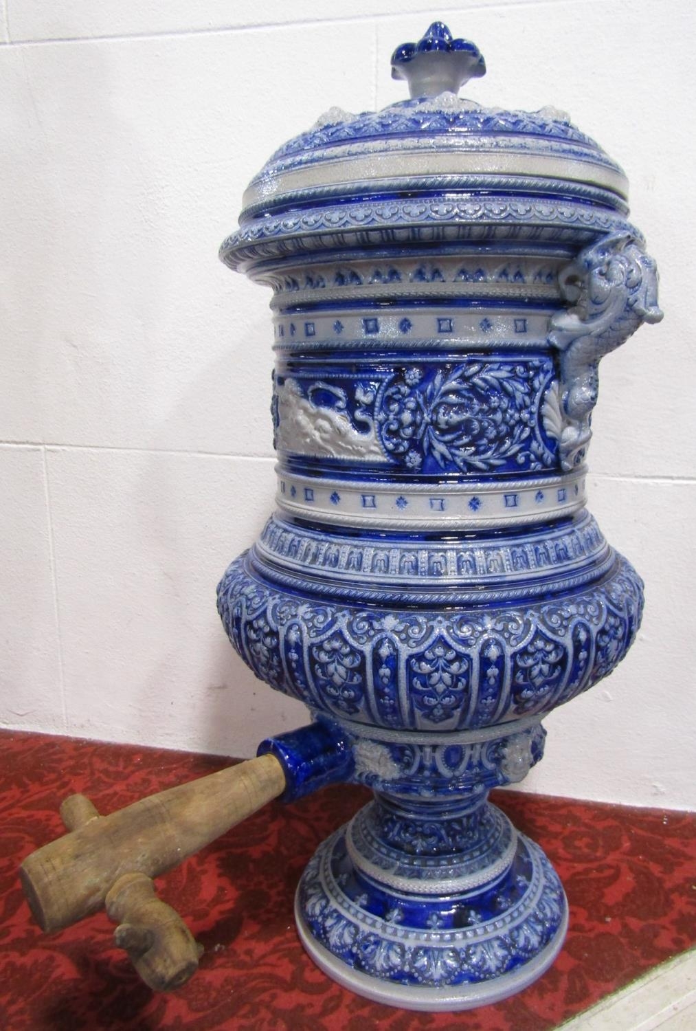 A large 19th century German stoneware relief moulded water dispenser and cover with handles modelled