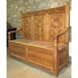 A pine settle with raised triple floral panelled back over open scrolled arms and box seat, with