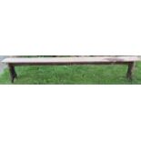A long vintage stained pine bench with rectangular plank seat, raised on through jointed shaped