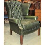 A Georgian style wing library chair with scrolled arms upholstered in green leather, with buttoned