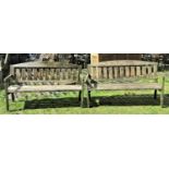 A pair of weathered softwood three seat garden benches with slatted seats and backs beneath arched