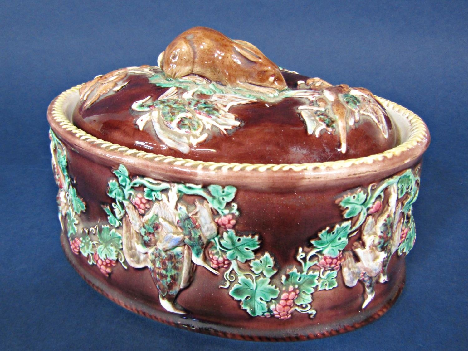 A 19th century majolica game dish and cover with relief moulded game bird and fruiting vine detail