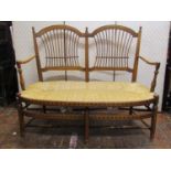 A late 19th century beechwood two seat settee with arts and crafts influence with turned supports,