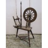 A traditional spinning wheel in oak raised on three turned supports, with foot treadle