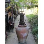 A weathered terracotta garden urn with moulded loop handles and containing a well established