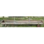 A portable galvanised steel feeding trough with cast iron wheels and raised central rail, 9ft long