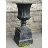 A cast iron campana shaped urn with flared egg and dart rim, fluted and lobed body and raised on a