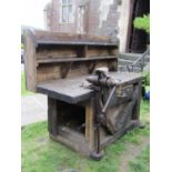 A vintage and rustic workshop bench of thick pine boarded construction, raised and shelved back over