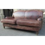 A traditional two seat sofa, upholstered in a mid tan coloured leather, raised on turned supports,