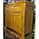 A contemporary pale oak side cupboard enclosed by two panelled doors and two frieze drawers on swept