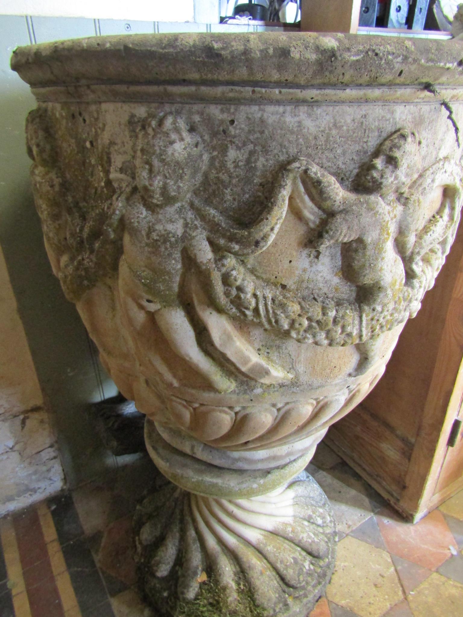 A reclaimed garden urn of circular form with raised repeating cherub and swag detail raised on a