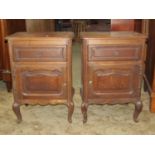 A pair of panelled oak bedside or drawing room tables, each enclosed by a cupboard door and drawer