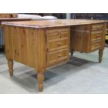 A pine kneehole writing desk fitted with an arrangement of three graduated drawers and a cupboard (