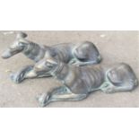 A pair of composition stone garden ornaments in the form of recumbent greyhounds/whippets, with