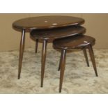 An Ercol dark elm and beechwood nest of 'pebble' occasional tables raised on simple tapered stick