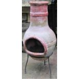 A weathered chimenea raised on a simple iron work stand, 92 cm high