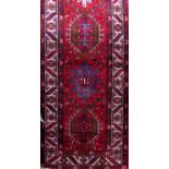 A good long Heriz runner with faceted floral and other medallion patterns upon a red ground, 420 x