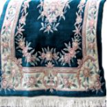 A Chinese wool full pile rug with typical floral decoration in relief upon a bottled green ground,