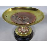 Continental brass and copper musical tazza, the inset copper relief panel decorated with a stag,
