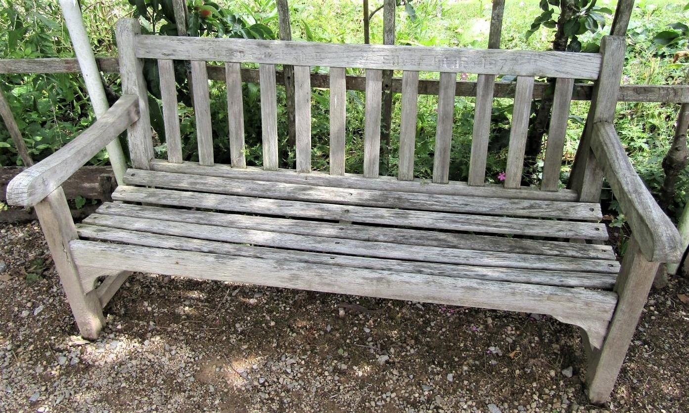 A weathered teak wood garden bench to commemorate the 1977 Silver Jubilee, 153cm wide