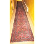 A very long eastern wool runner with repeating floral detail upon a salmon pink ground within narrow