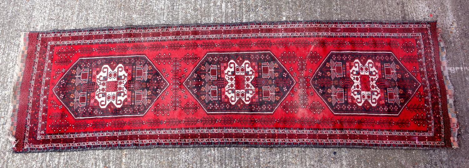 Oriental carpet runner, with three central medallions, on a deep red ground, 274 x 78 cm