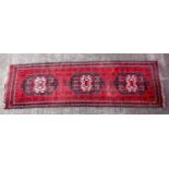 Oriental carpet runner, with three central medallions, on a deep red ground, 274 x 78 cm