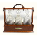 Late Victorian oak tantalus with silver plated mounts and three wrythen and cut glass decanters, (