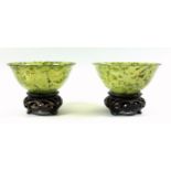 A pair of modern Oriental jadeite/glass bowls, each with mottled inclusions, on hardwood bases, bowl
