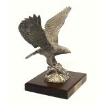 Silver model of an eagle naturalistically sculpted with its wings upstretched, perched on a rocky