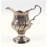 George III silver helmet shaped cream jug with floral embossed decoration and scroll handle, on a