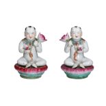 A pair of polychrome porcelain sculptures depicting boys on lotus petals with a pomegranate and
