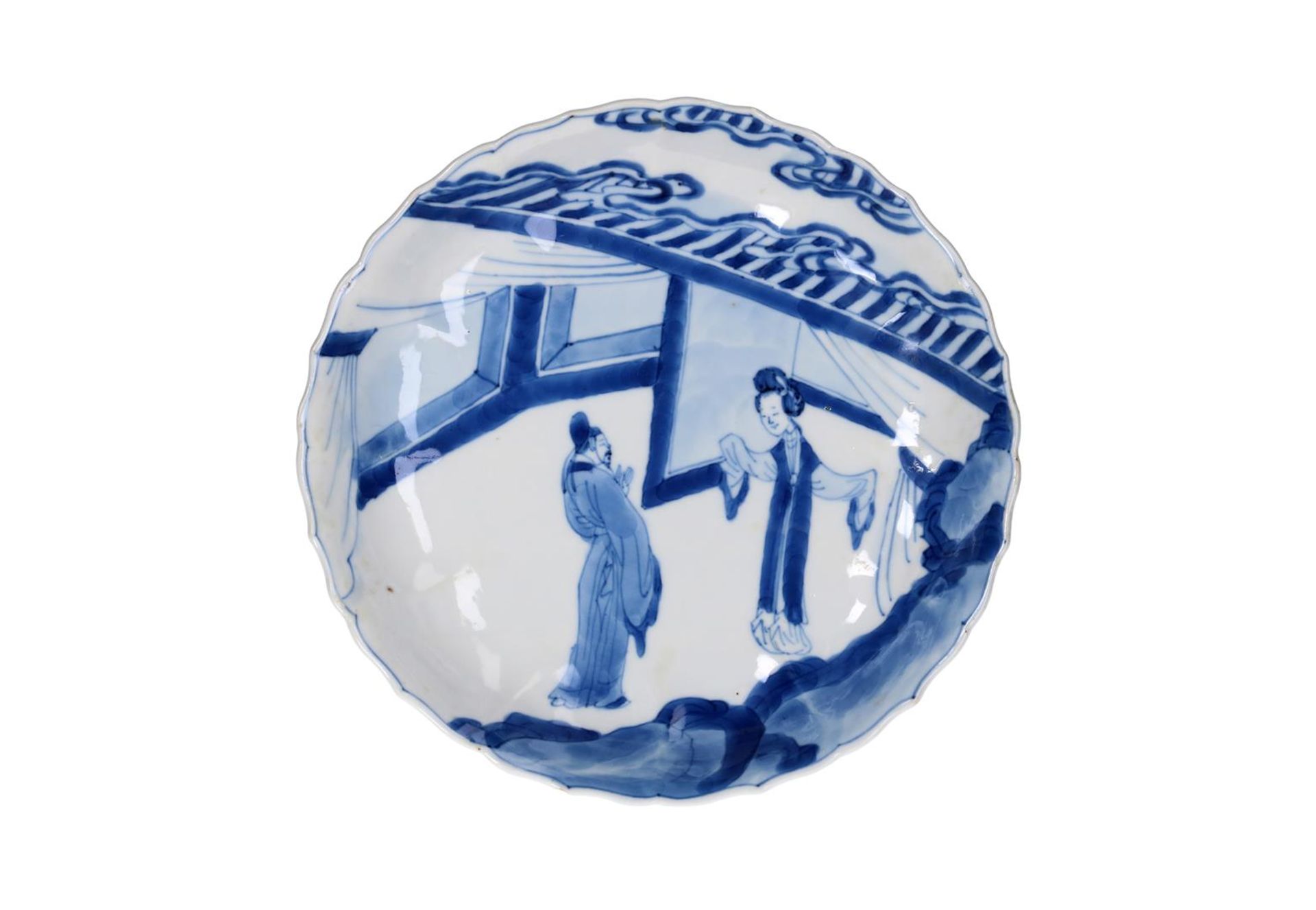 A blue and white porcelain plate with a serrated edge, decorated with figures in a pavilion.