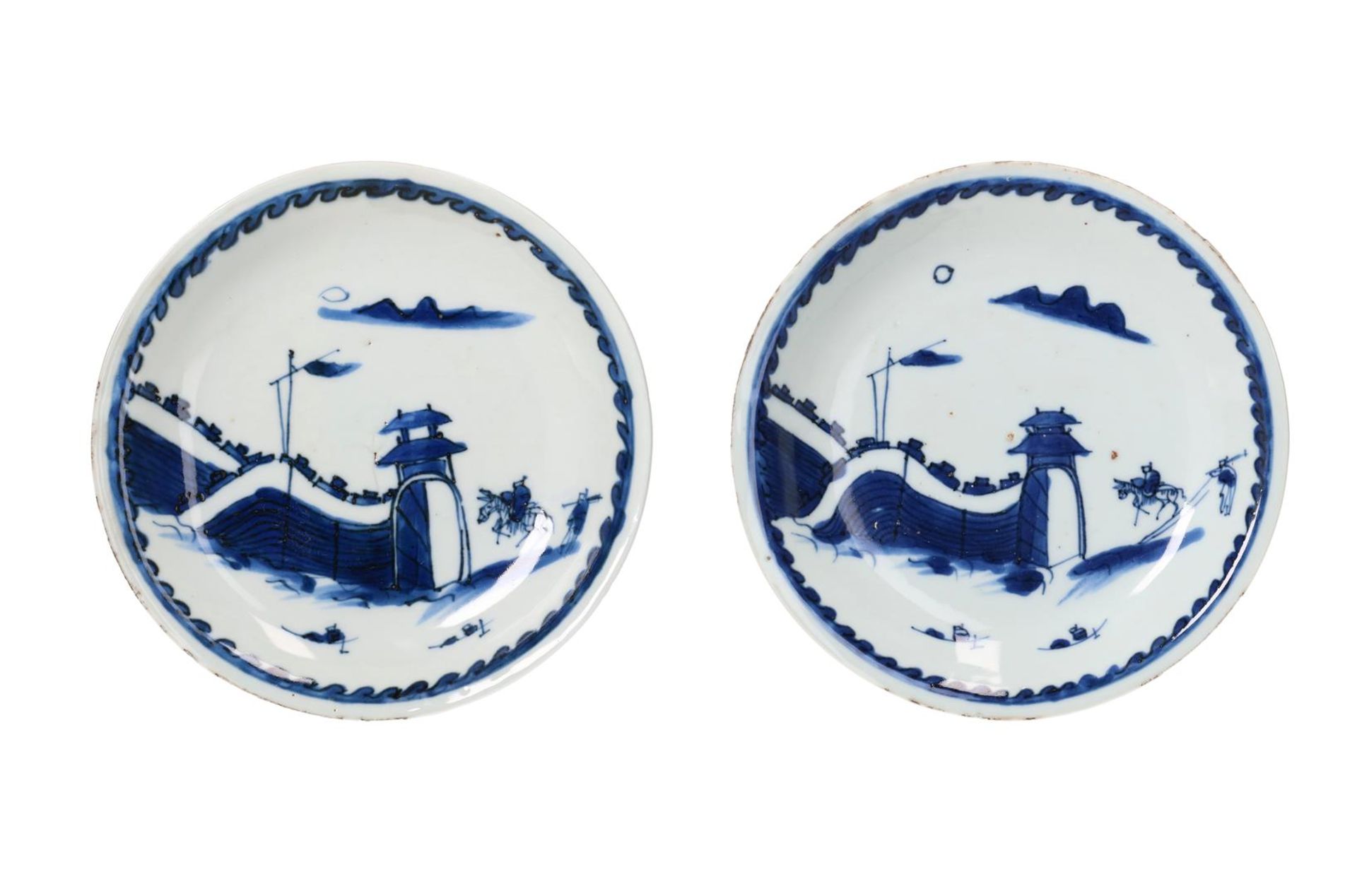 A pair of blue and white porcelain saucers, decorated with two figures on horseback approaching a