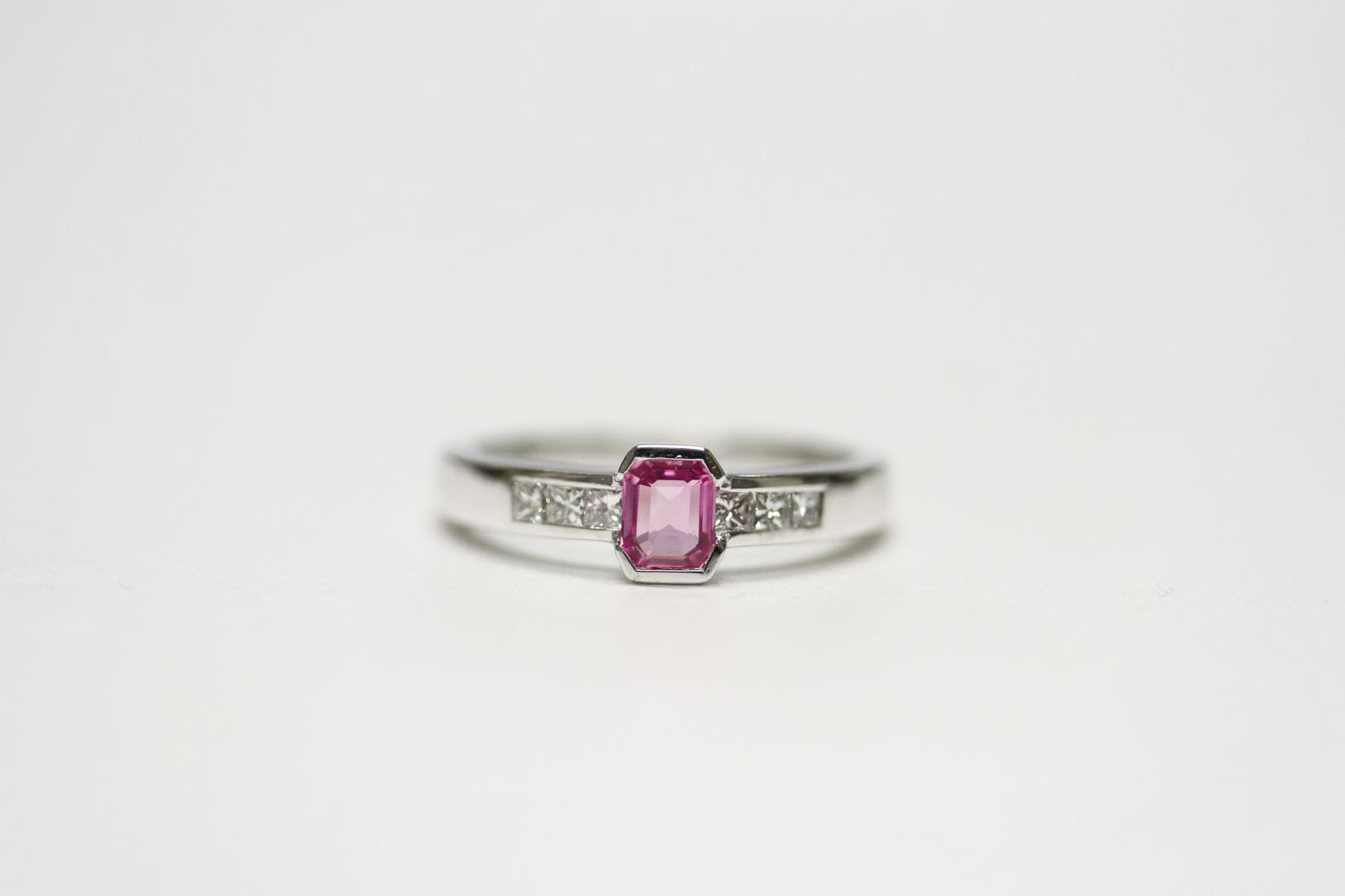 18ct white gold semi-rubover-set pink sapphire and channel-set diamond ring. Emerald-cut pink