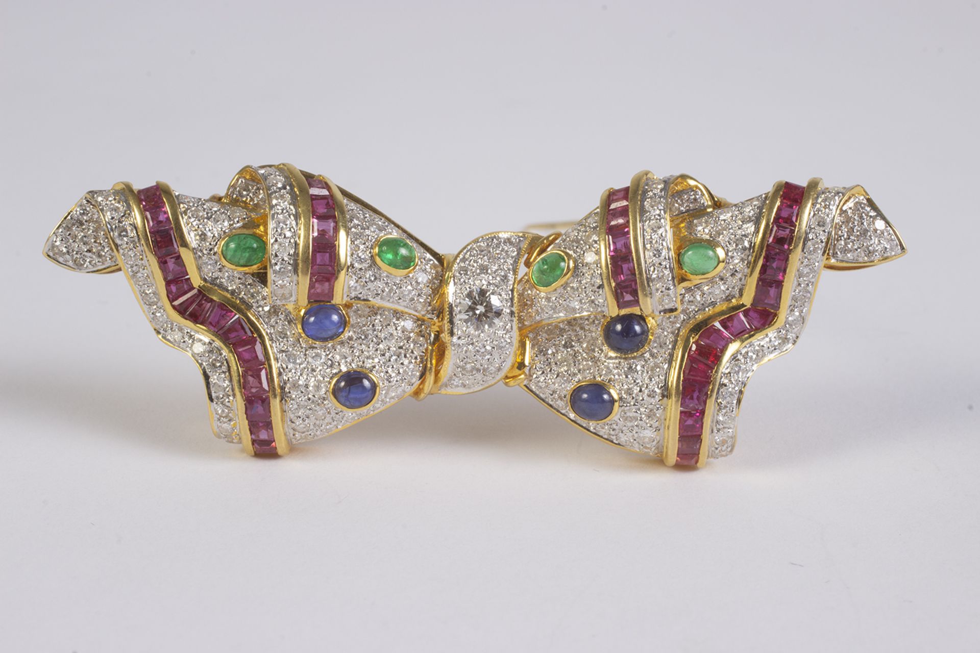 Broche en forma de lazo en oro, diamantes talla brillante, esmeralda., zafiros azules talla cabujón