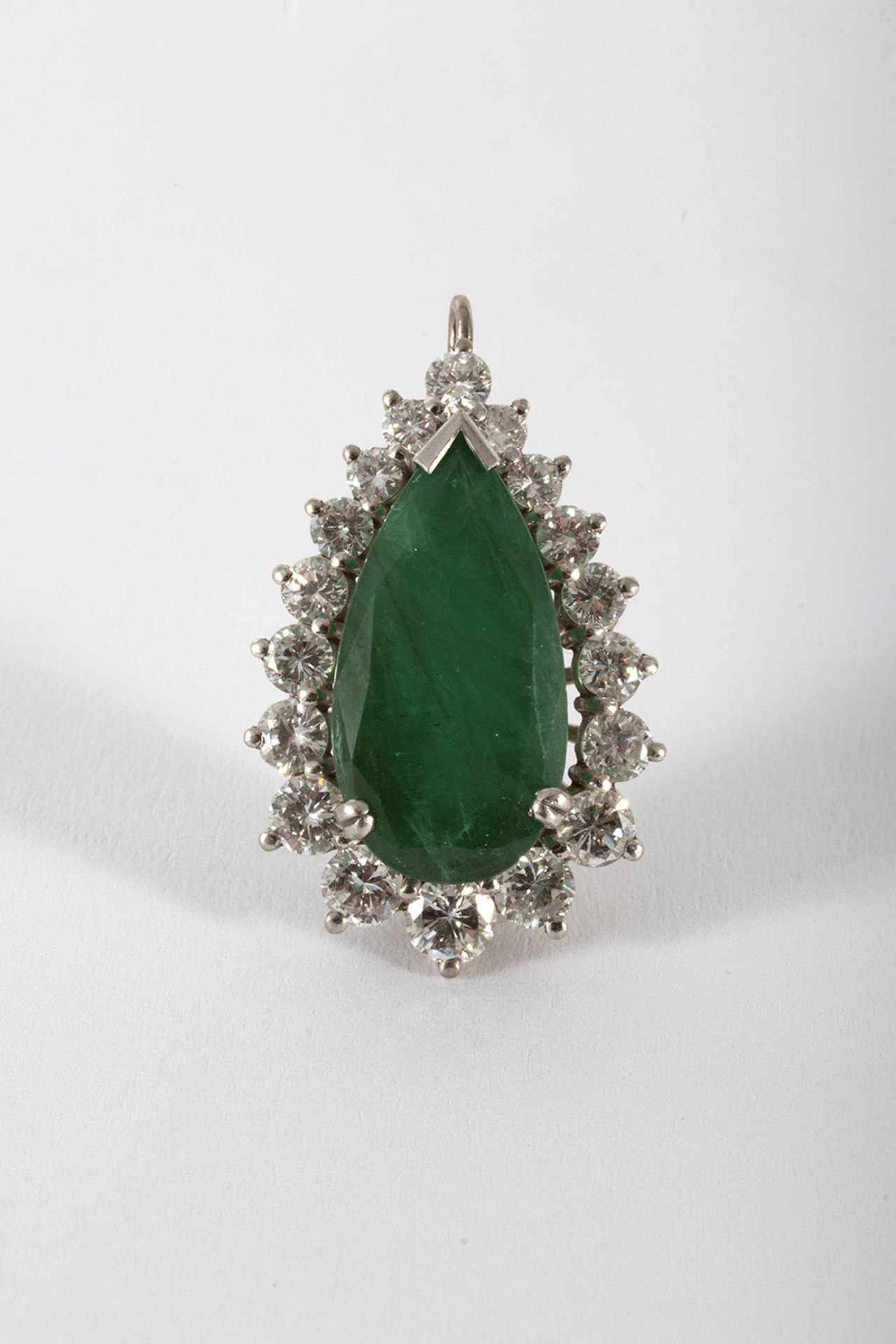 White gold pendant with a knob-cut emerald and a brilliant-cut diamond border.