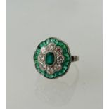Platinum emerald and diamond dress ring. Set with a central emerald, a floral halo of diamonds,