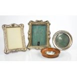 Three silver photograph frames, one embossed with scrollwork decoration.