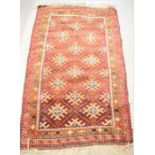 A Middle Eastern red ground wool rug, with red ground and stylised diamond motifs.