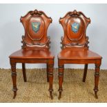 A pair of 19th century hall chairs with scroll work carving to the back, centred by shields