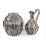 A large African water carrier and ewer, bound in rope with handles.