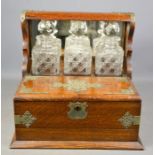 A Victorian oak and silver plated tantalus, with three glass decanters, with two lift up covers