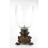 A large glass candle holder, with a faux-wood base depicting bows, floral garlands and raised on