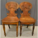 A pair of 19th century oak hall chairs with scroll carved backs.